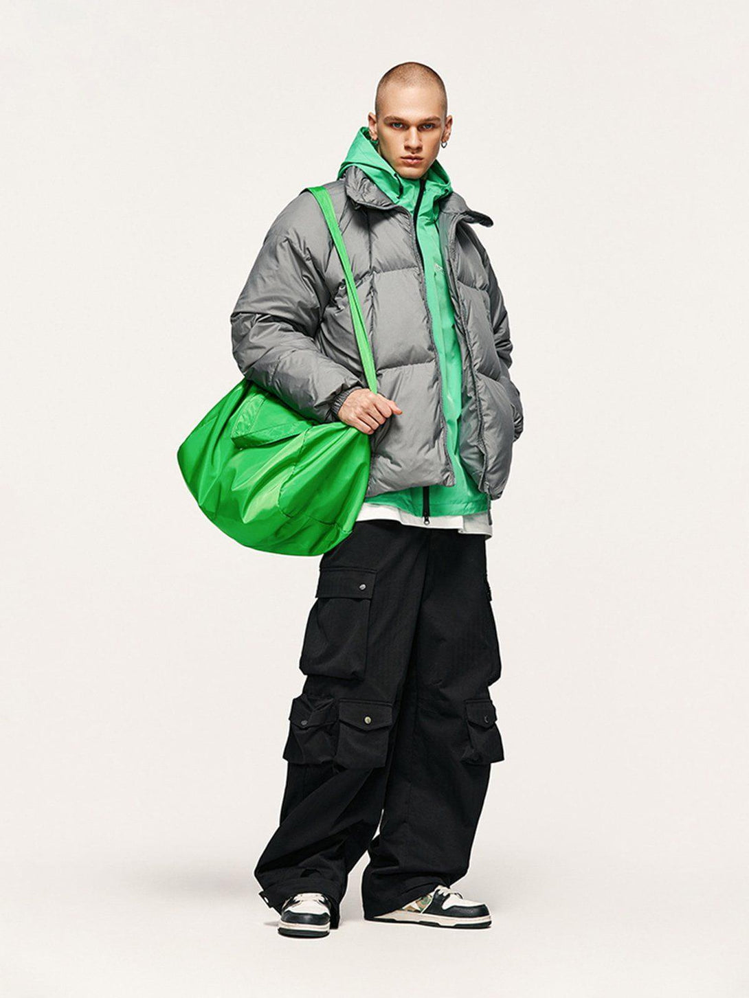 Model in gray puffer and black TALISHKO 3D cargo pants, accented with a vibrant green bag.