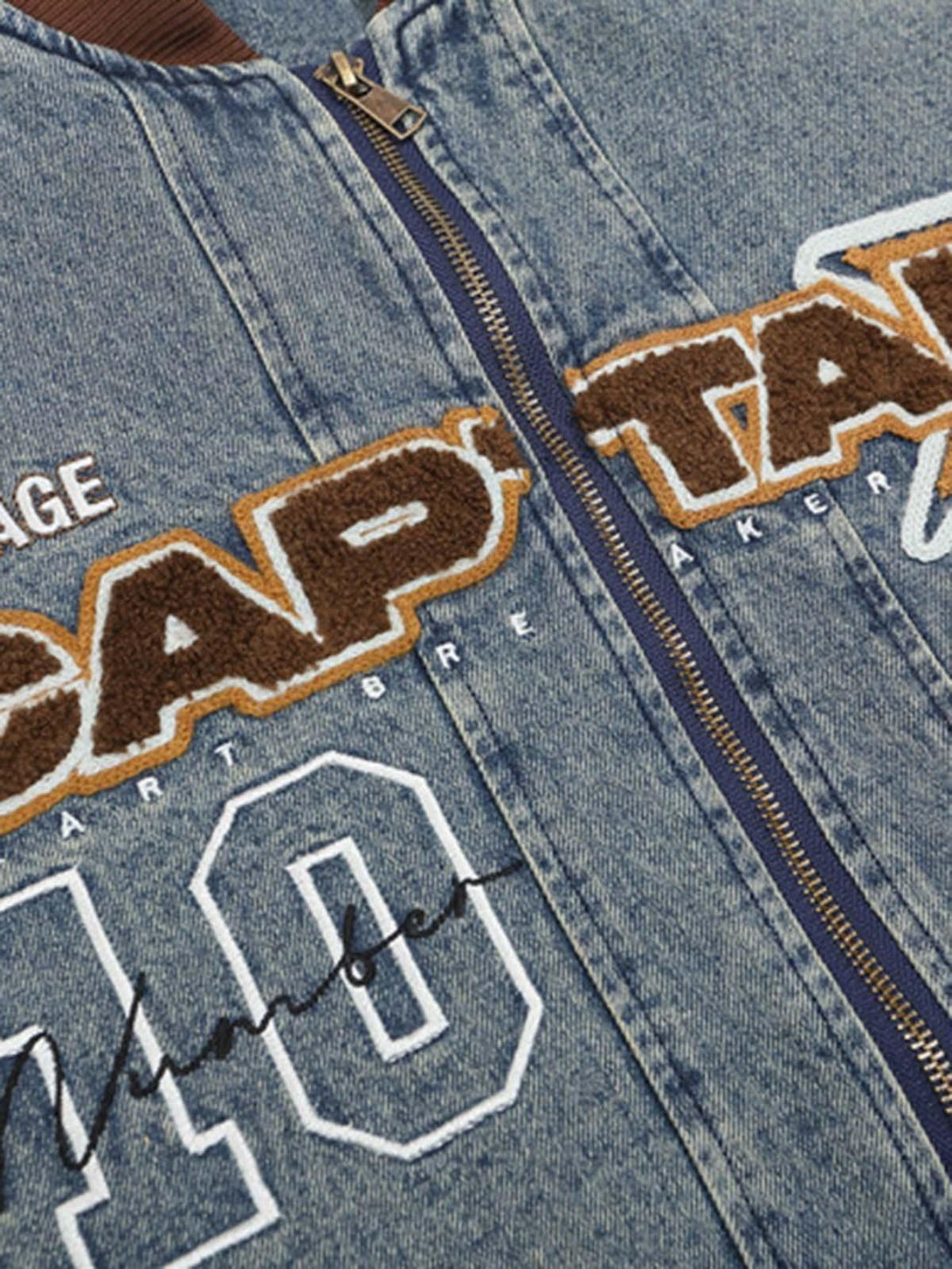 Denim bomber jacket by TALISHKO showcasing embroidered patches and quilted details up close.