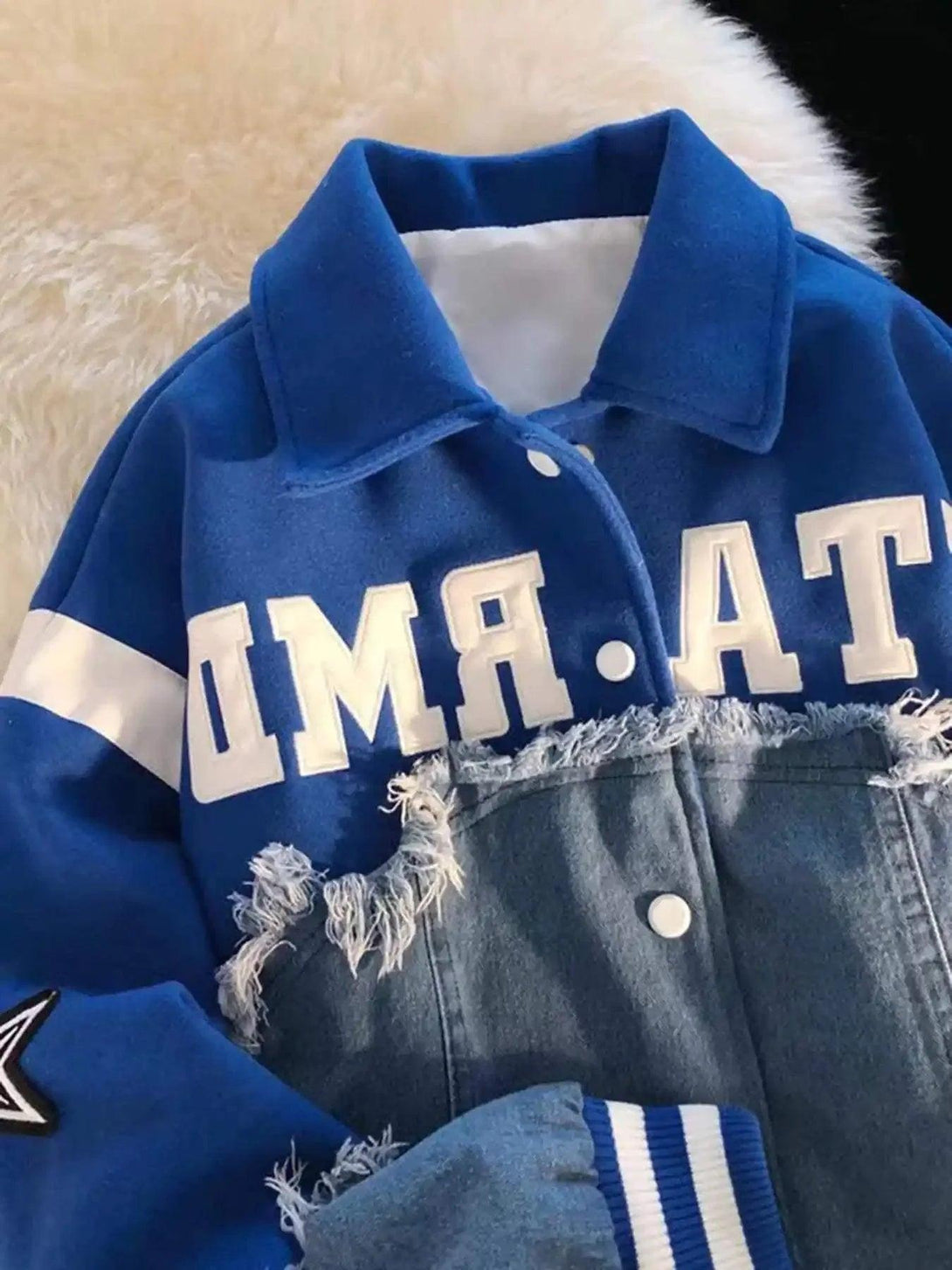 A close-up of TALISHKO's blue denim splicing baseball jacket, highlighting frayed details and bold lettering.