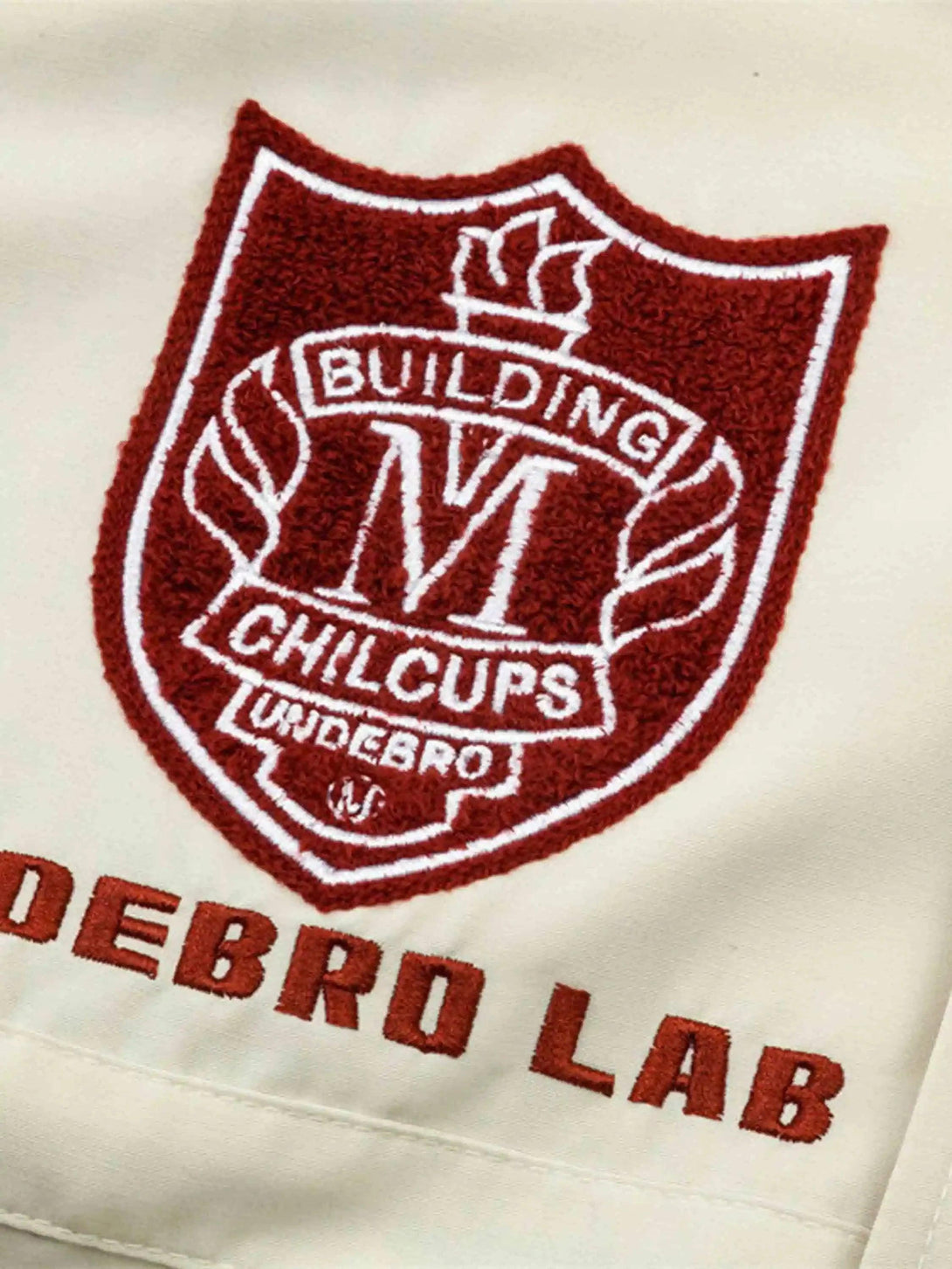 Intricate look at TALISHKO's varsity patch embroidery on a cream baseball jacket, highlighting campus style.