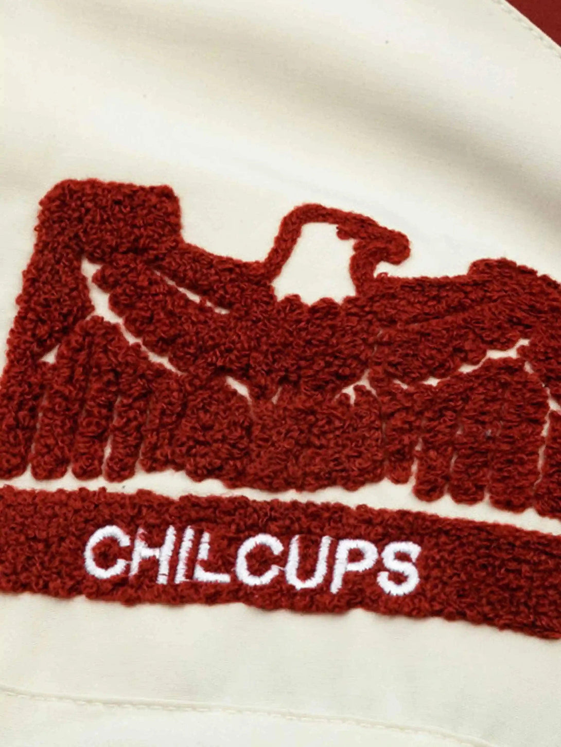 Intricate embroidery detail of TALISHKO's cream baseball jacket showcasing hip-hop campus style.