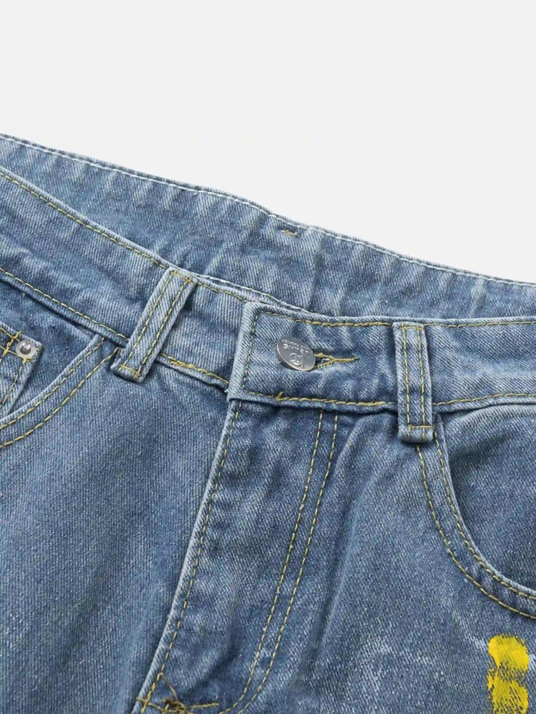 A detailed view of TALISHKO jeans, showcasing blue denim with artistic yellow paint accents.