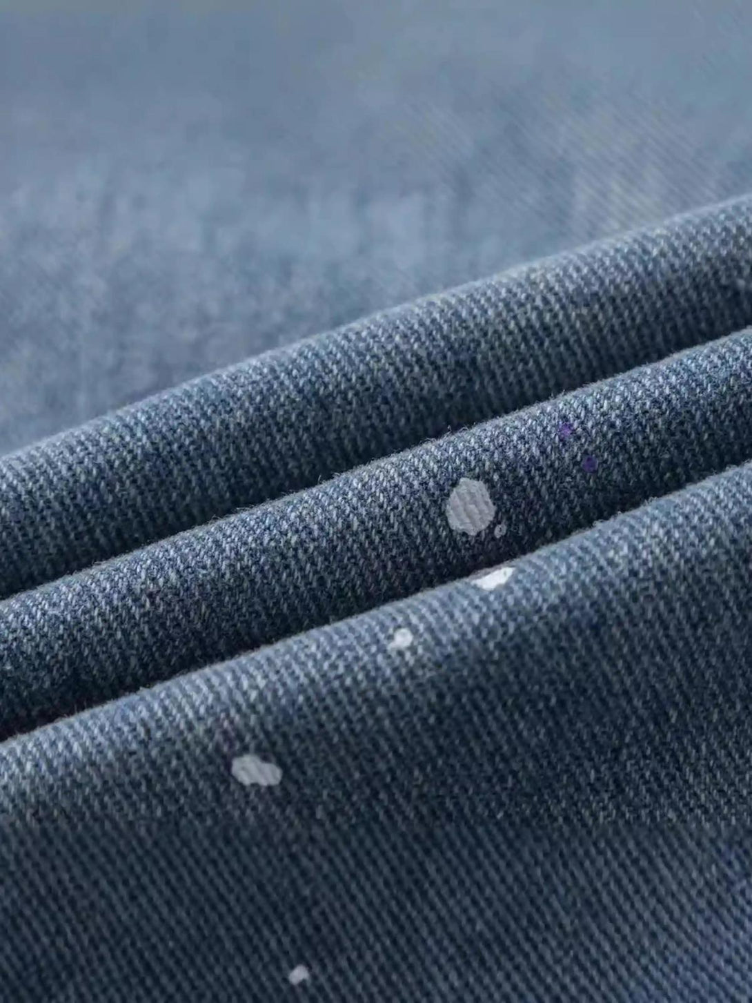 A close-up of TALISHKO jeans, highlighting the unique paint-splattered denim texture.