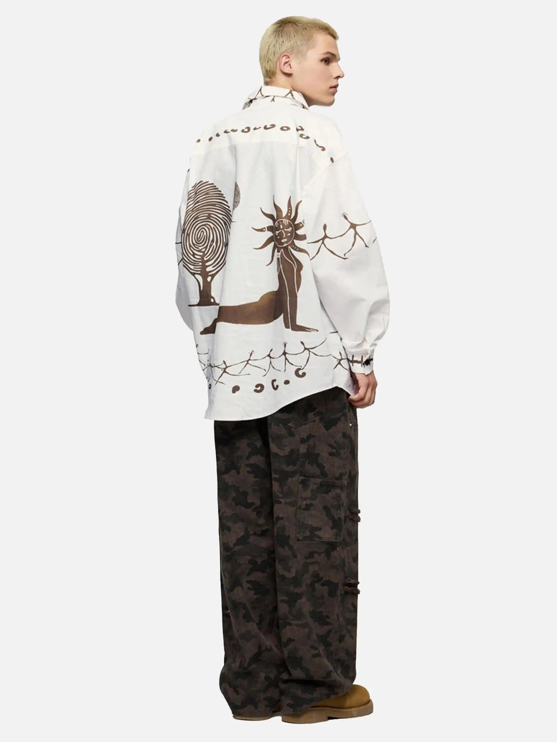 Model showcasing a TALISHKO mural shirt with abstract designs, paired with camo pants, side view.