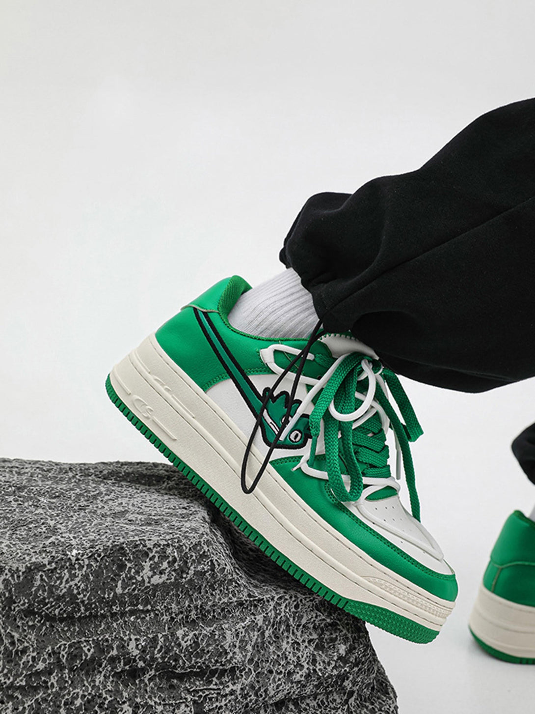 Green TALISHKO sneakers with bold design, shown styled with black pants on a rocky surface.
