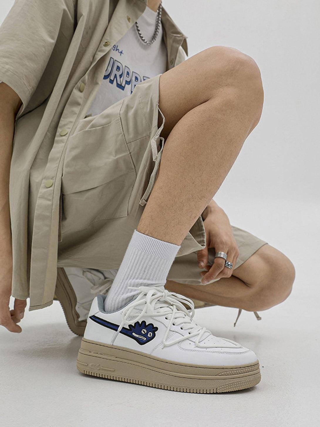 Model wearing TALISHKO white sneakers with monster design, styled with beige shorts.