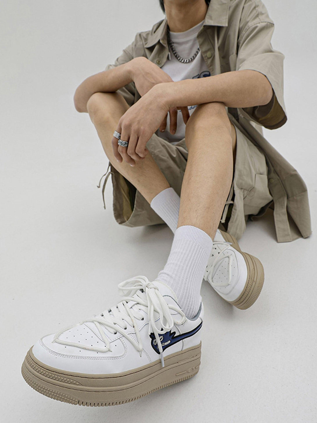 Model wearing white TALISHKO sneakers with monster design, paired with beige outfit and socks.