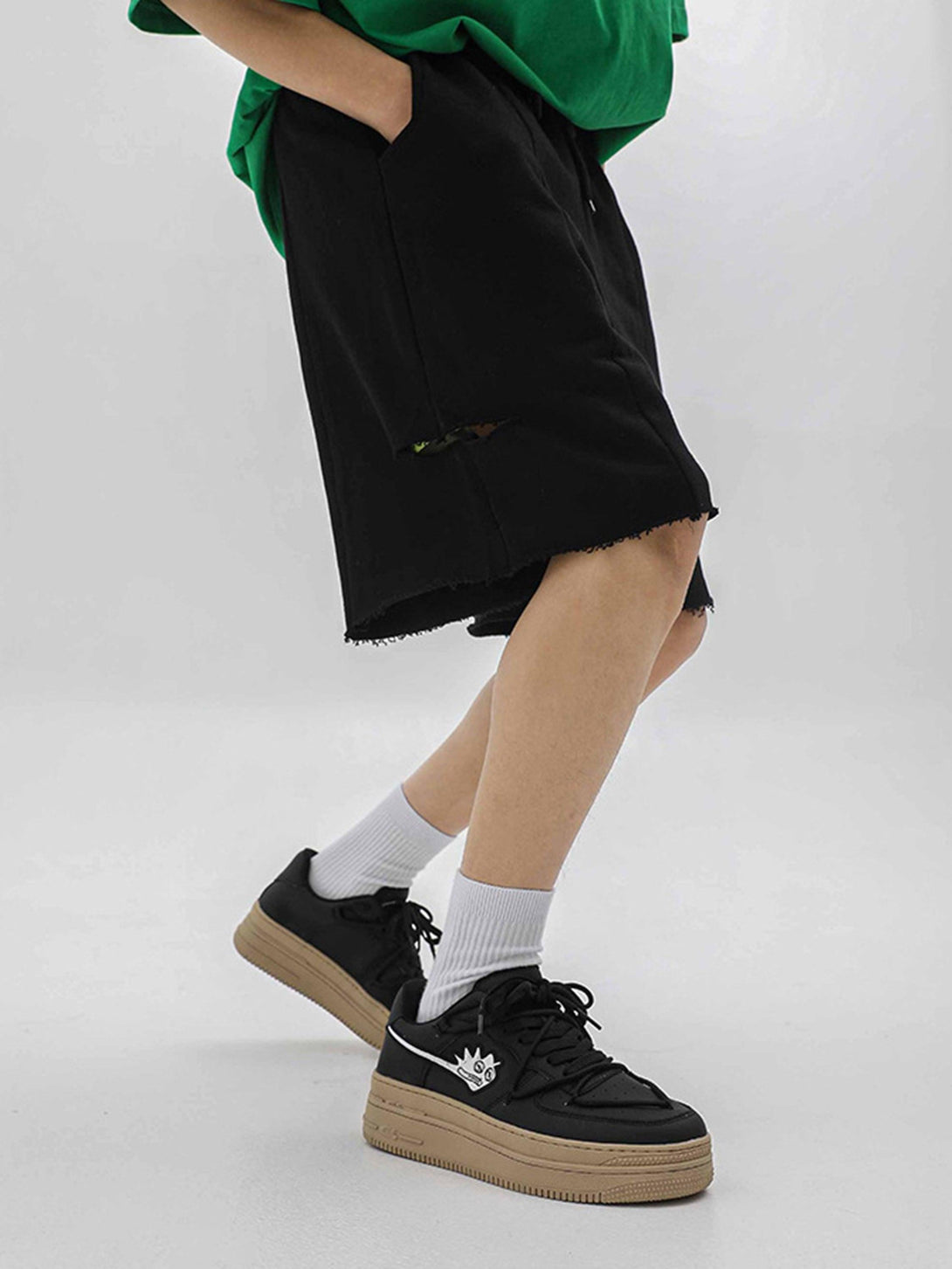 Model wearing black TALISHKO sneakers with monster design, paired with black shorts and socks.