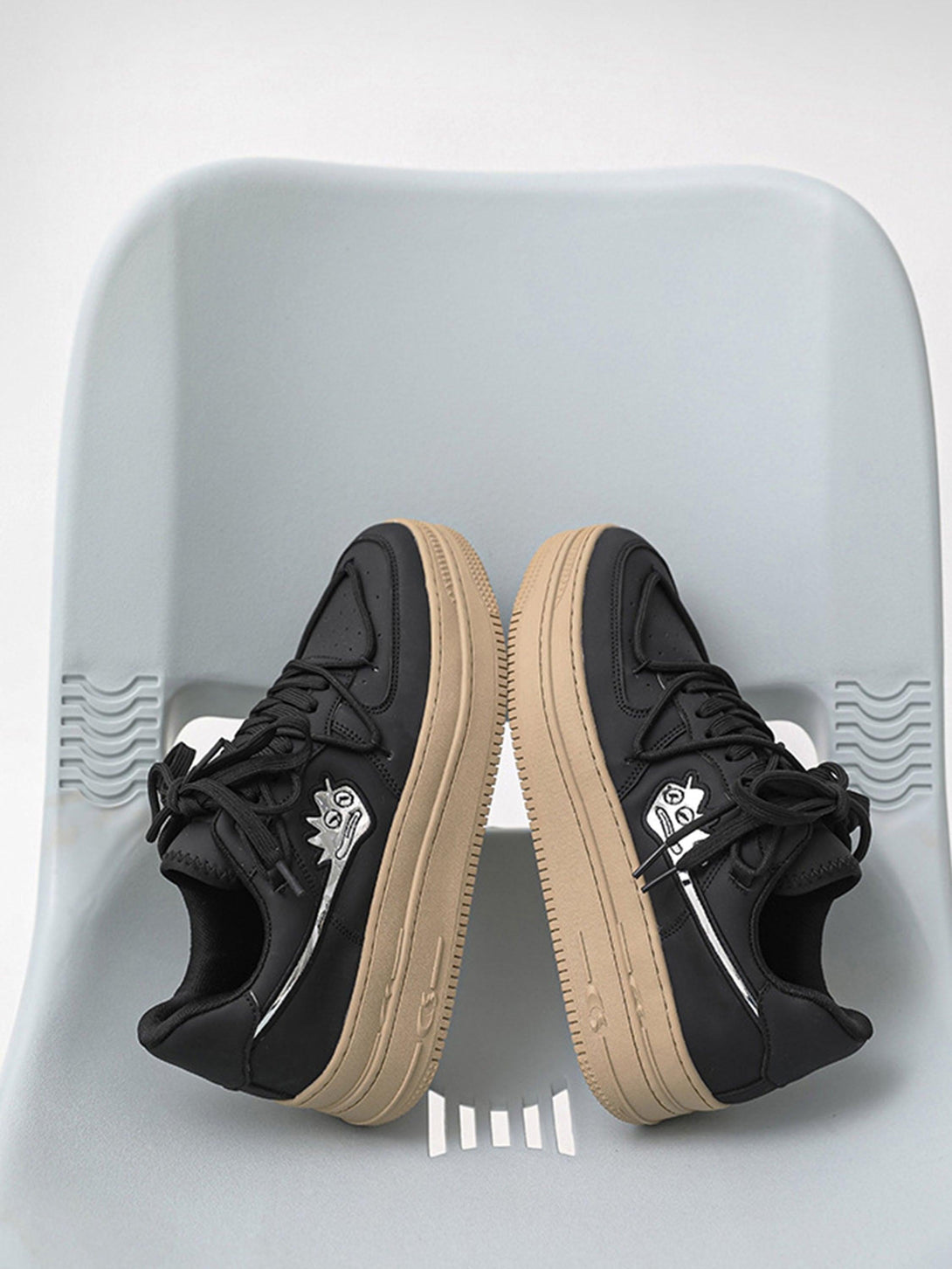 Black TALISHKO sneakers with beige soles featuring a monster graphic, displayed on a chair.