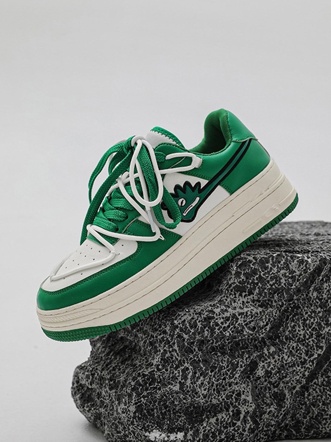 Green and white TALISHKO sneakers with monster design, displayed on a textured rock backdrop.
