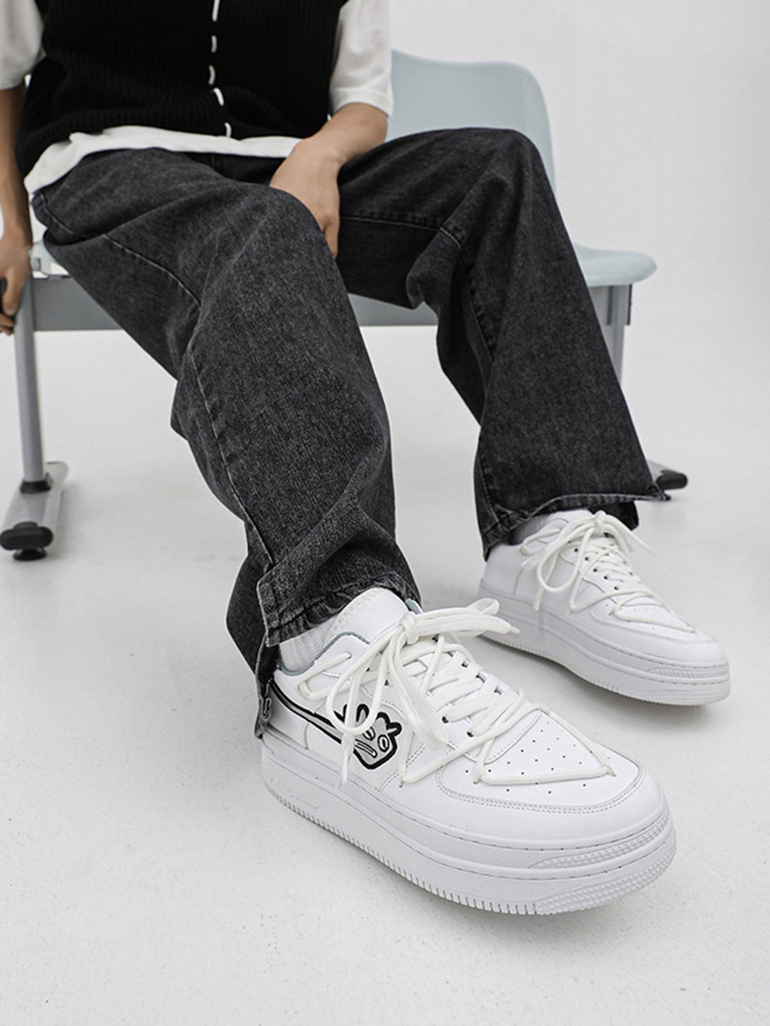 Model wearing TALISHKO white sneakers with monster design, styled with black denim jeans.