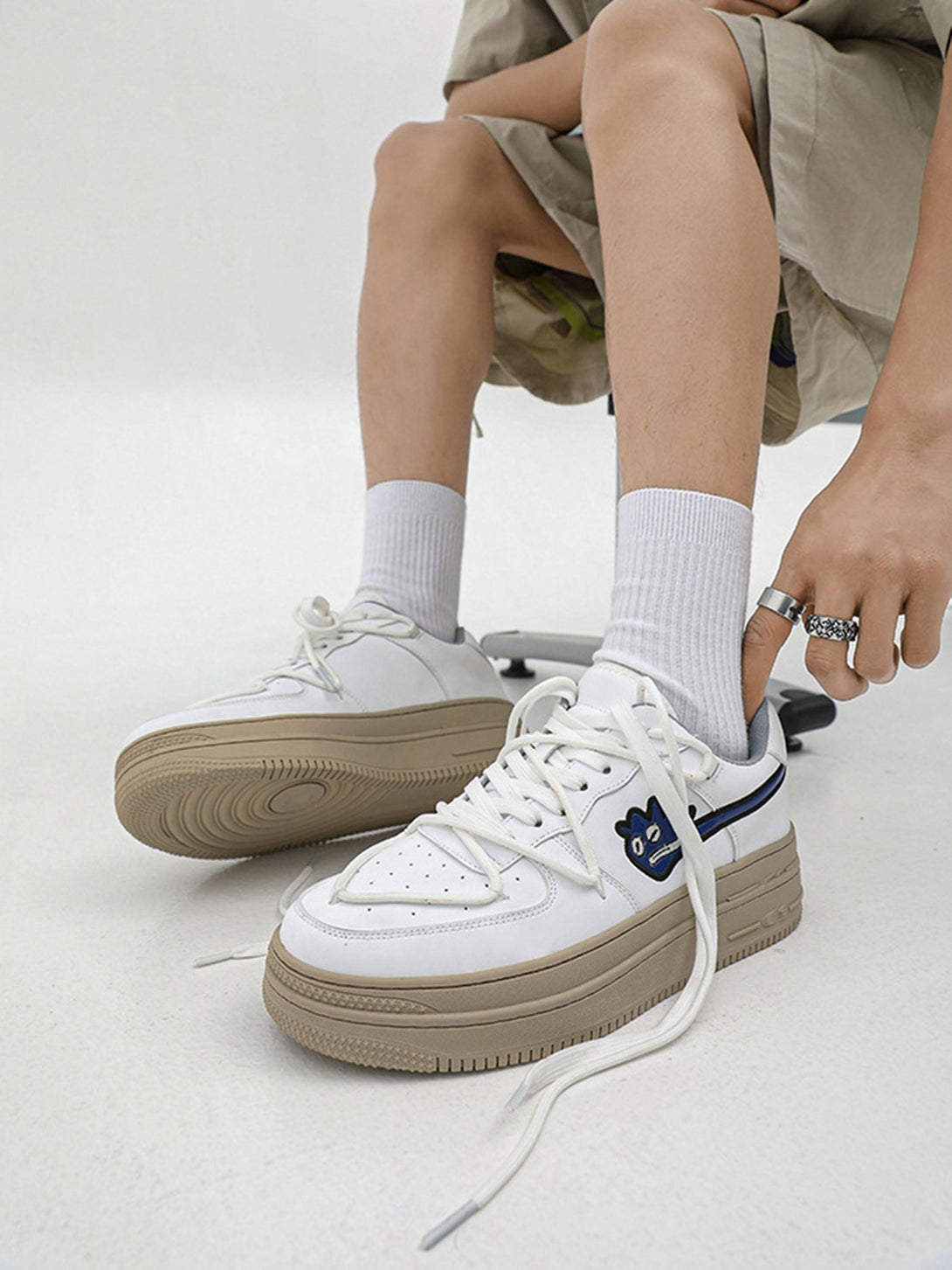 Model wearing white TALISHKO sneakers with monster design and beige soles, paired with shorts.