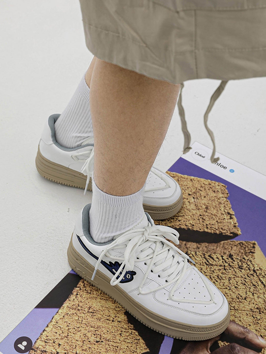 Model sporting white TALISHKO sneakers with monster design, paired with beige shorts and socks.