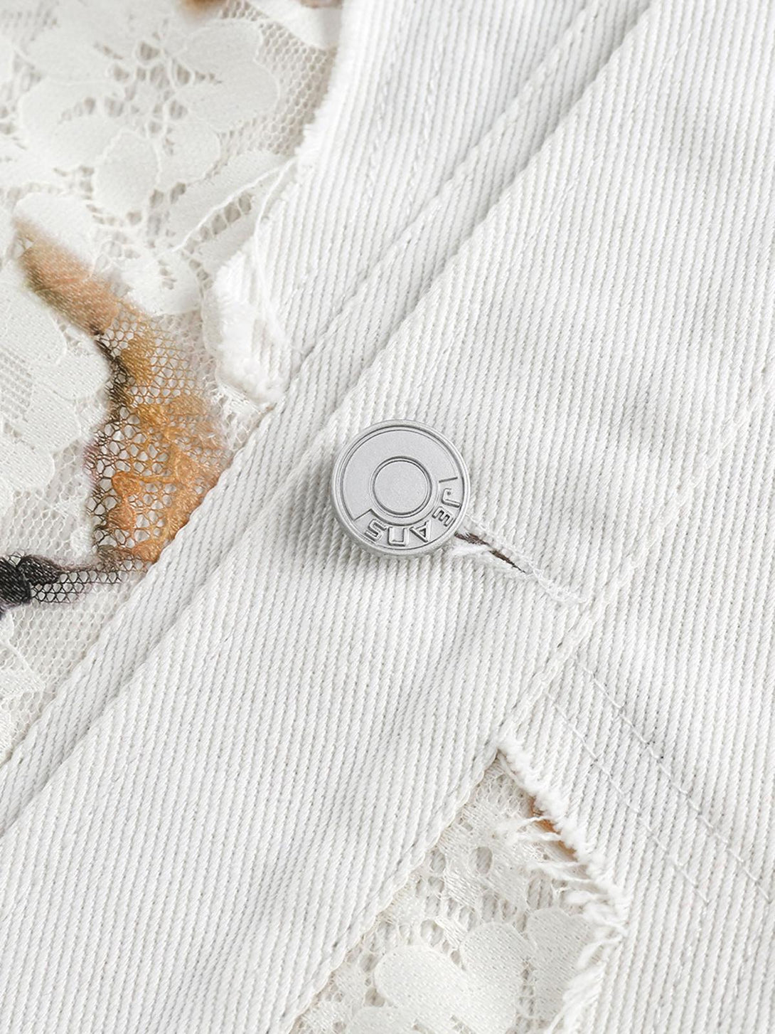 A detailed view of TALISHKO's denim jacket button and lace patchwork, highlighting craftsmanship.