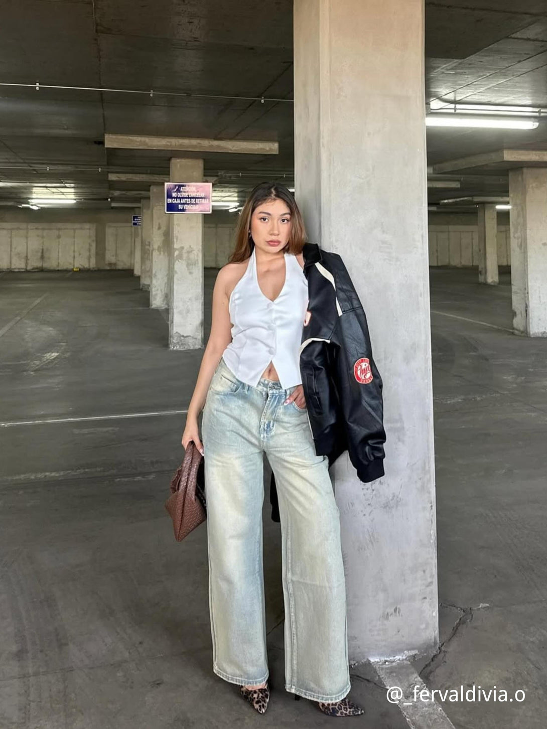 Model wearing a TALISHKO retro patchwork motorcycle jacket draped over shoulder, styled with wide-leg jeans.
