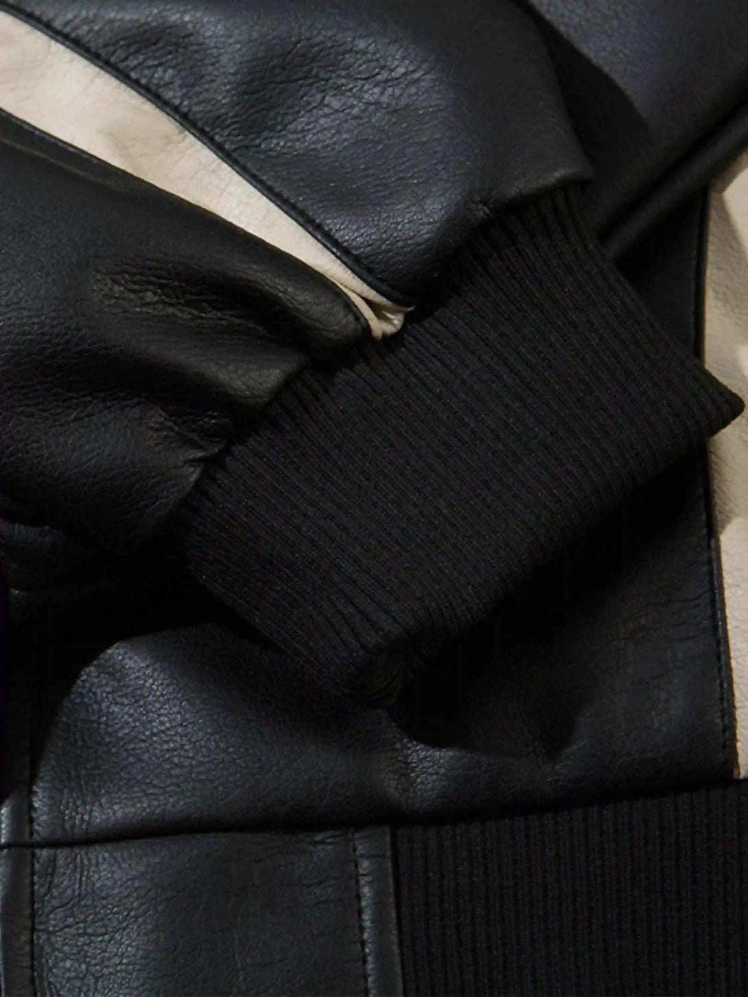 Detailed look at TALISHKO's black leather motorcycle jacket cuff and stitching.
