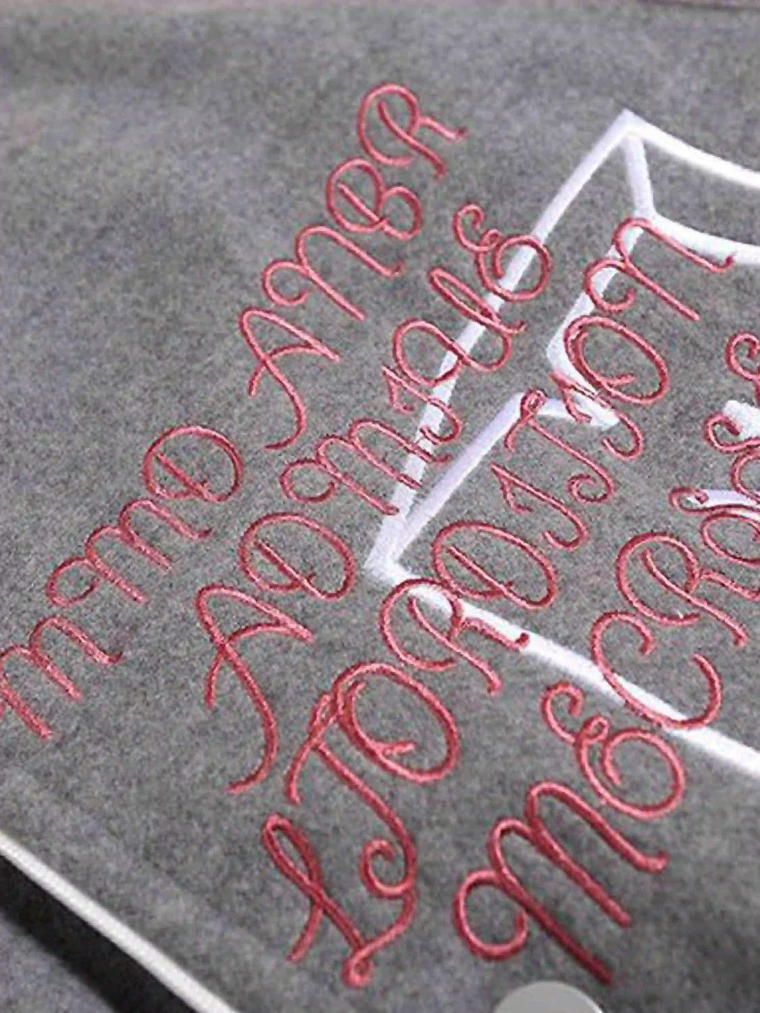 Intricate look at TALISHKO's woolen baseball jacket with red embroidered lettering on gray fabric.
