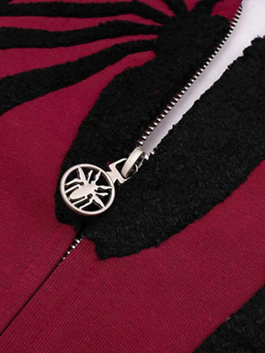 Detailed view of TALISHKO cardigan hoodie zipper with spider-themed embroidery on red fabric.