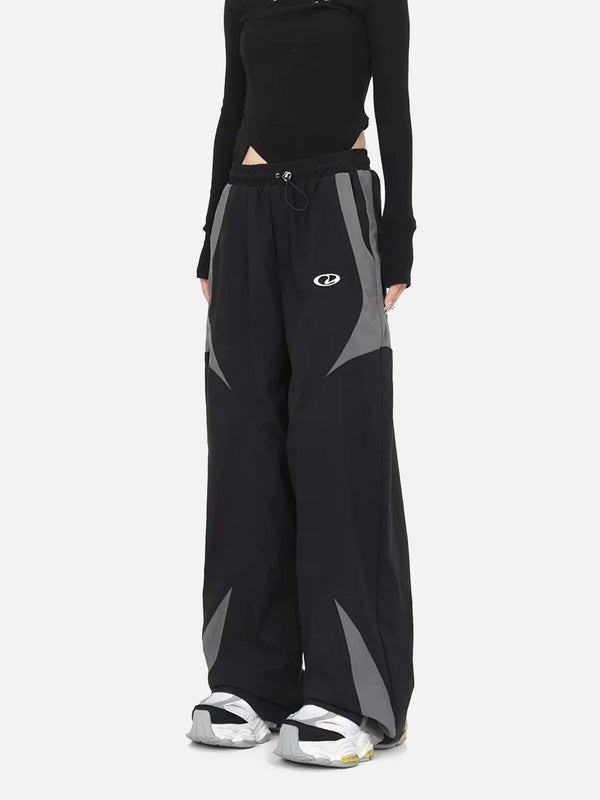 Model wearing TALISHKO casual black and gray sports pants with splicing design, showcasing street fashion style.