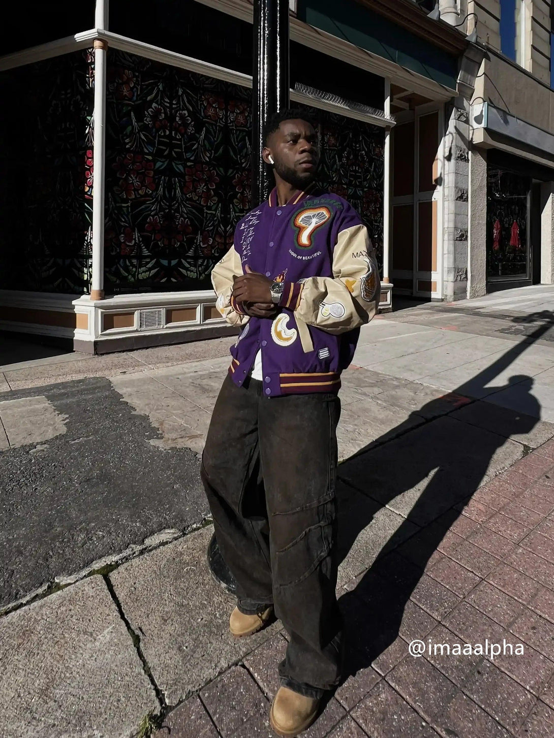 A man on a city street wears a TALISHKO retro baseball jacket with vibrant embroidery.