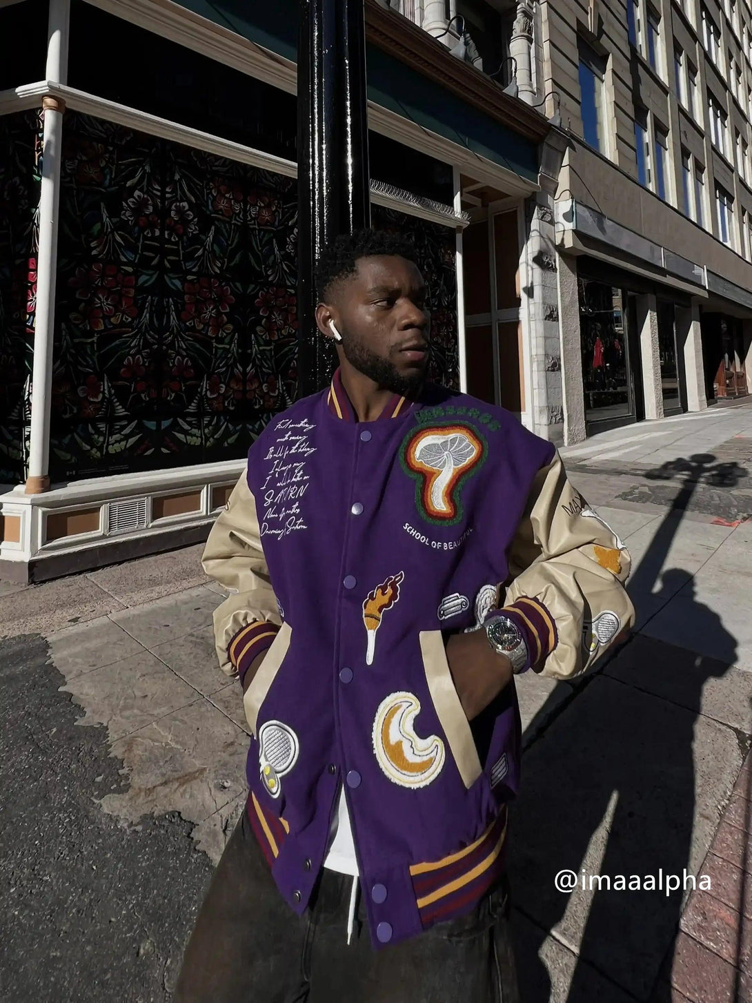 A man models the purple embroidered baseball jacket by TALISHKO on a city street.