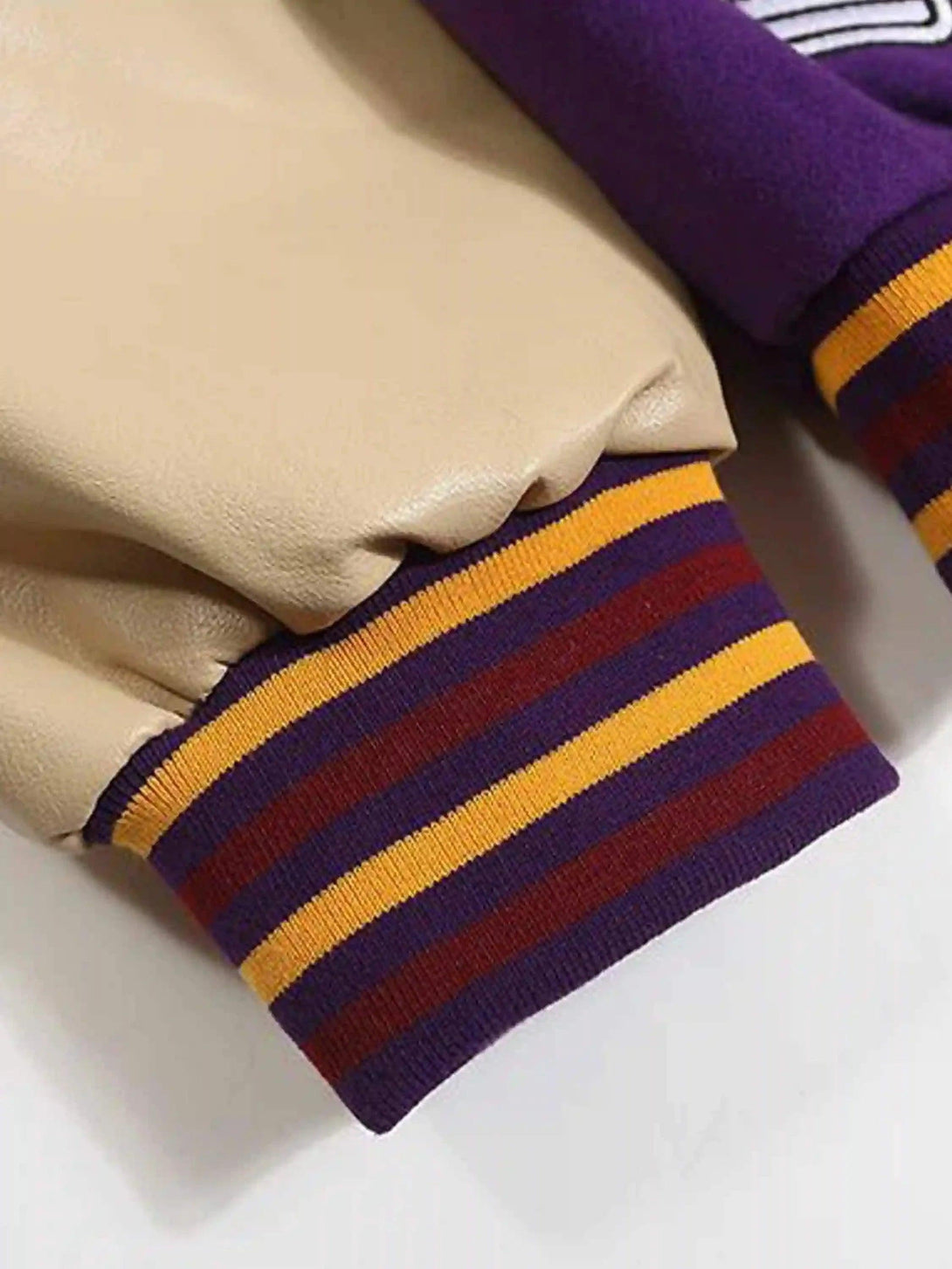 A detailed view of TALISHKO's baseball jacket cuff, featuring bold striped colors and textures.