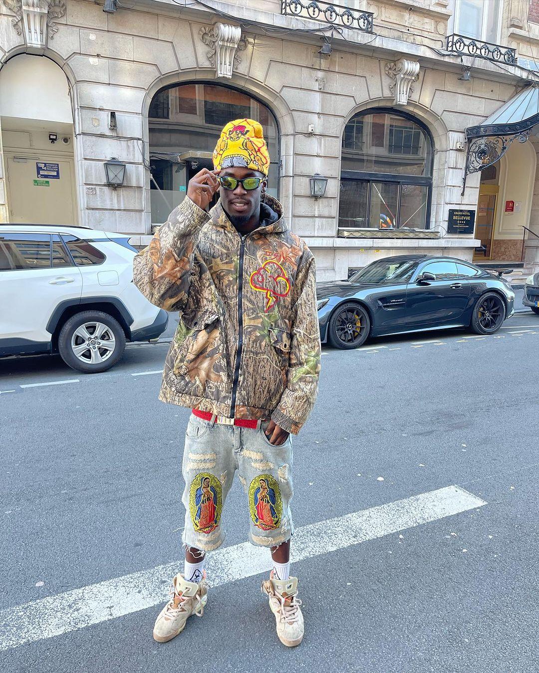 Model wearing TALISHKO's camo jacket and unique ripped jeans, showcasing vibrant street style.