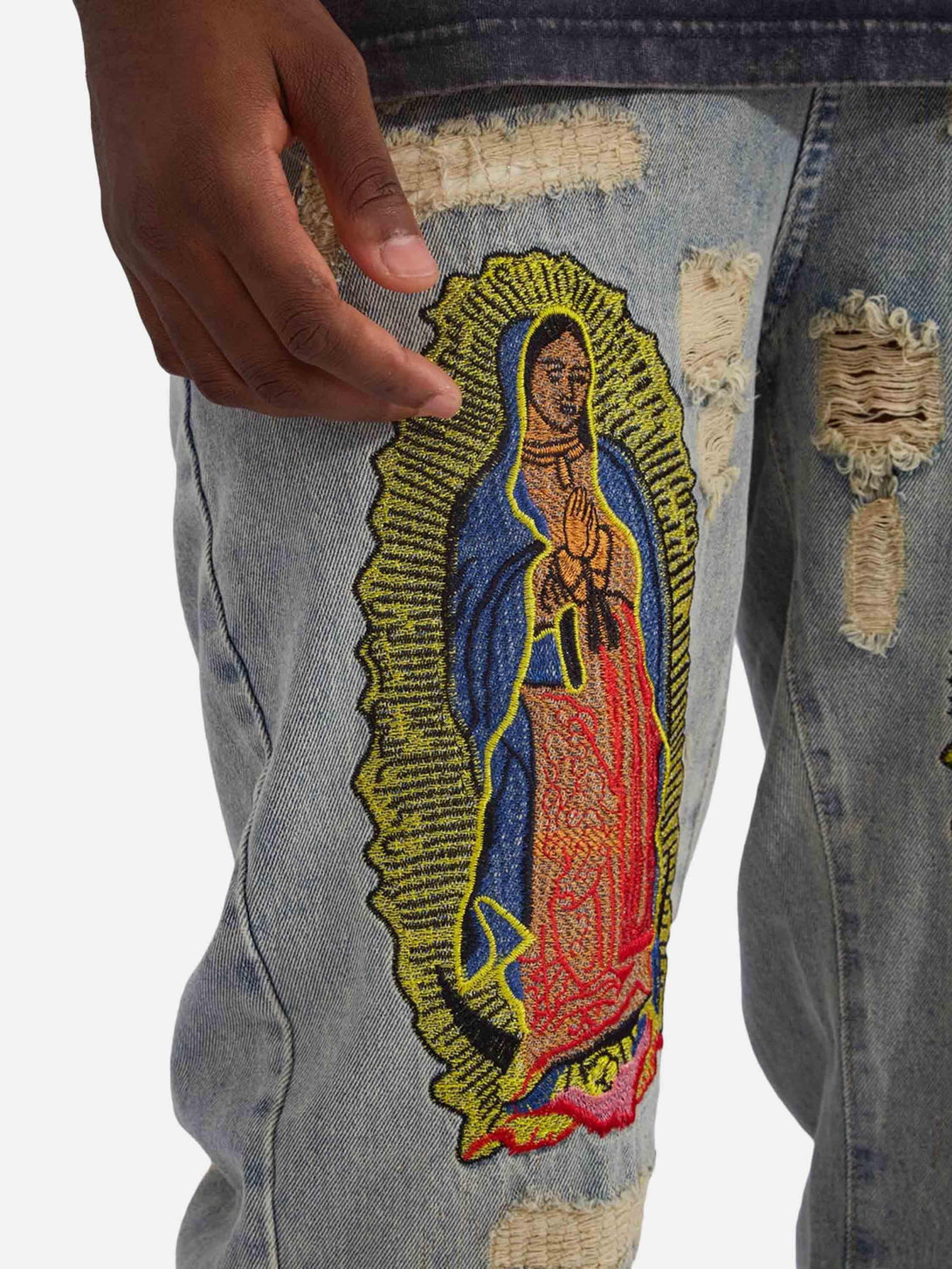 Zoomed-in detail of TALISHKO street-style jeans with religious patch and distressed texture.