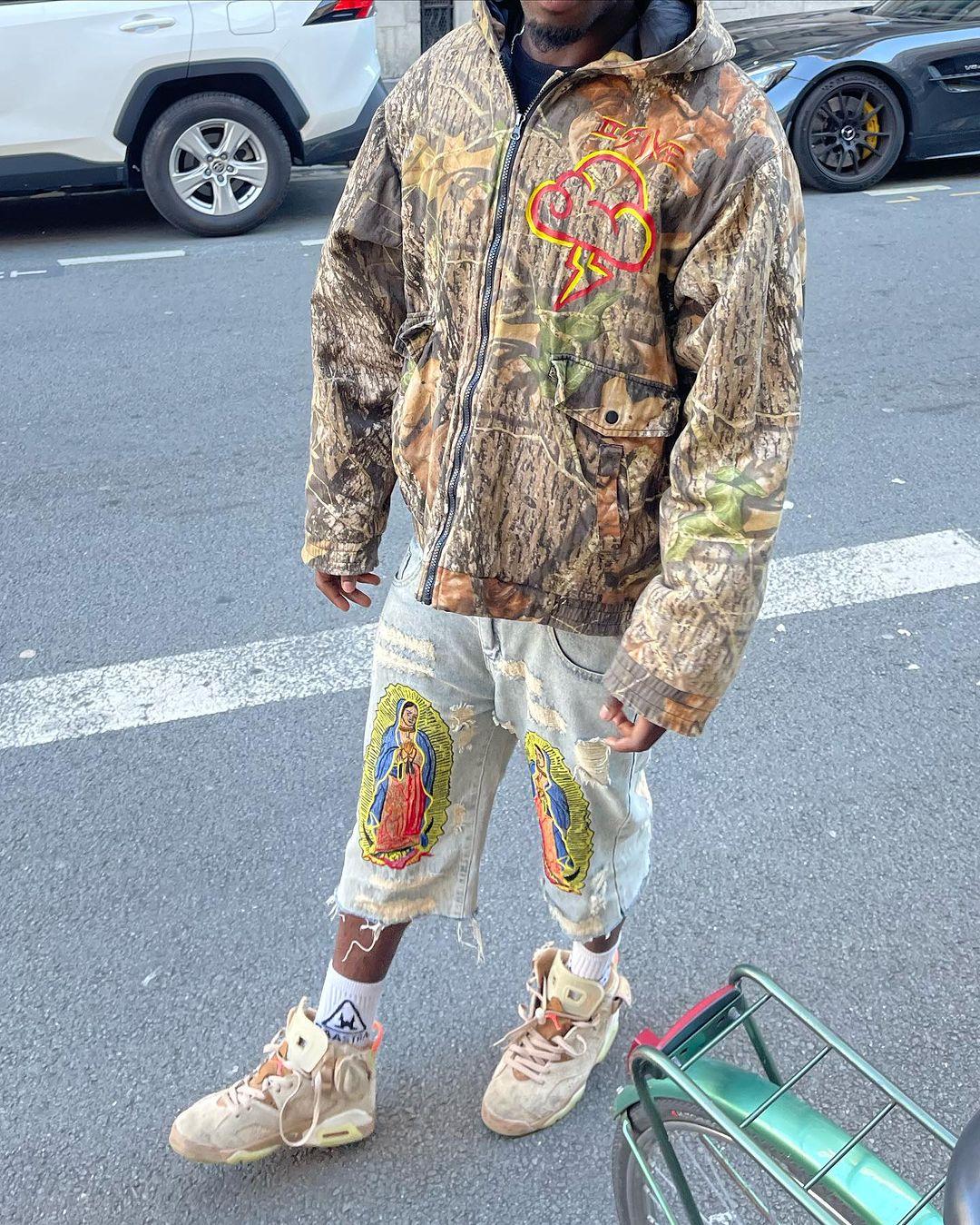 Urban streetwear look with TALISHKO camo jacket and ripped jeans featuring bold religious patches.