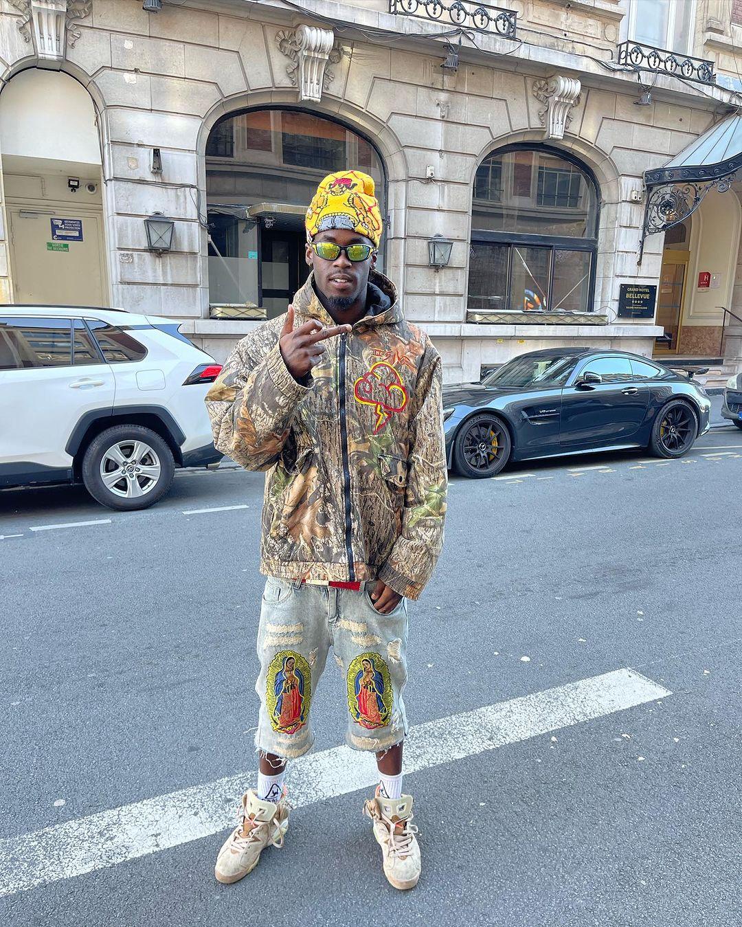 Street-style look in TALISHKO camo jacket and ripped jeans with religious patches, urban vibe.