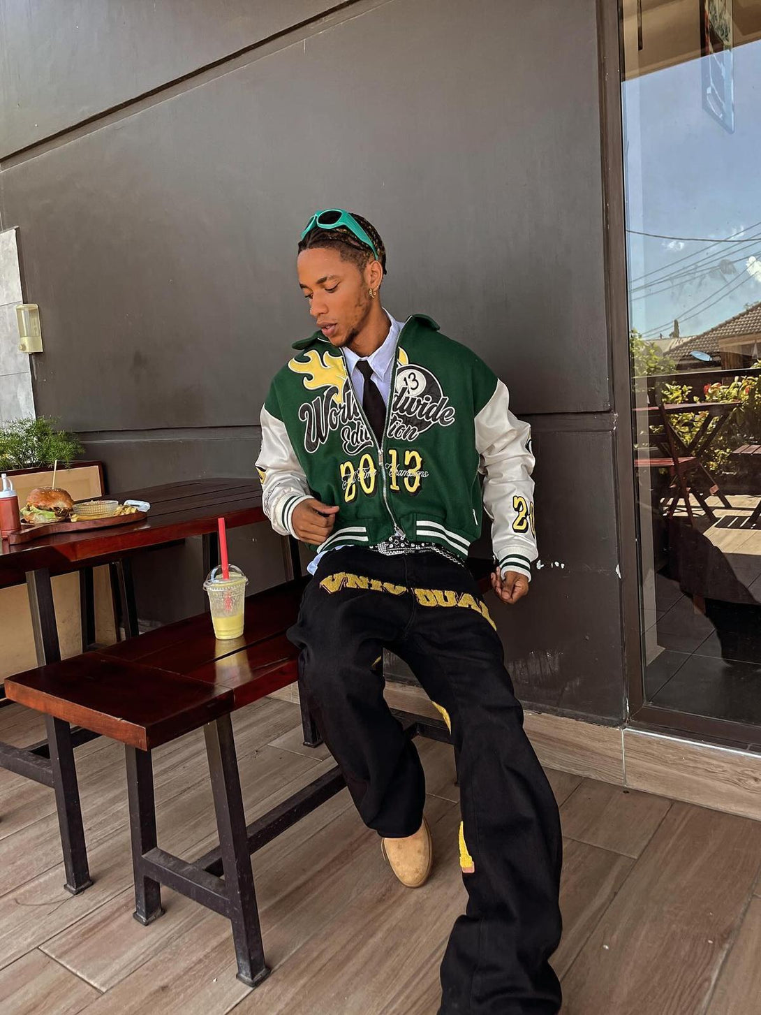 Model in TALISHKO varsity jacket and jeans, enjoying a casual day at an outdoor café.