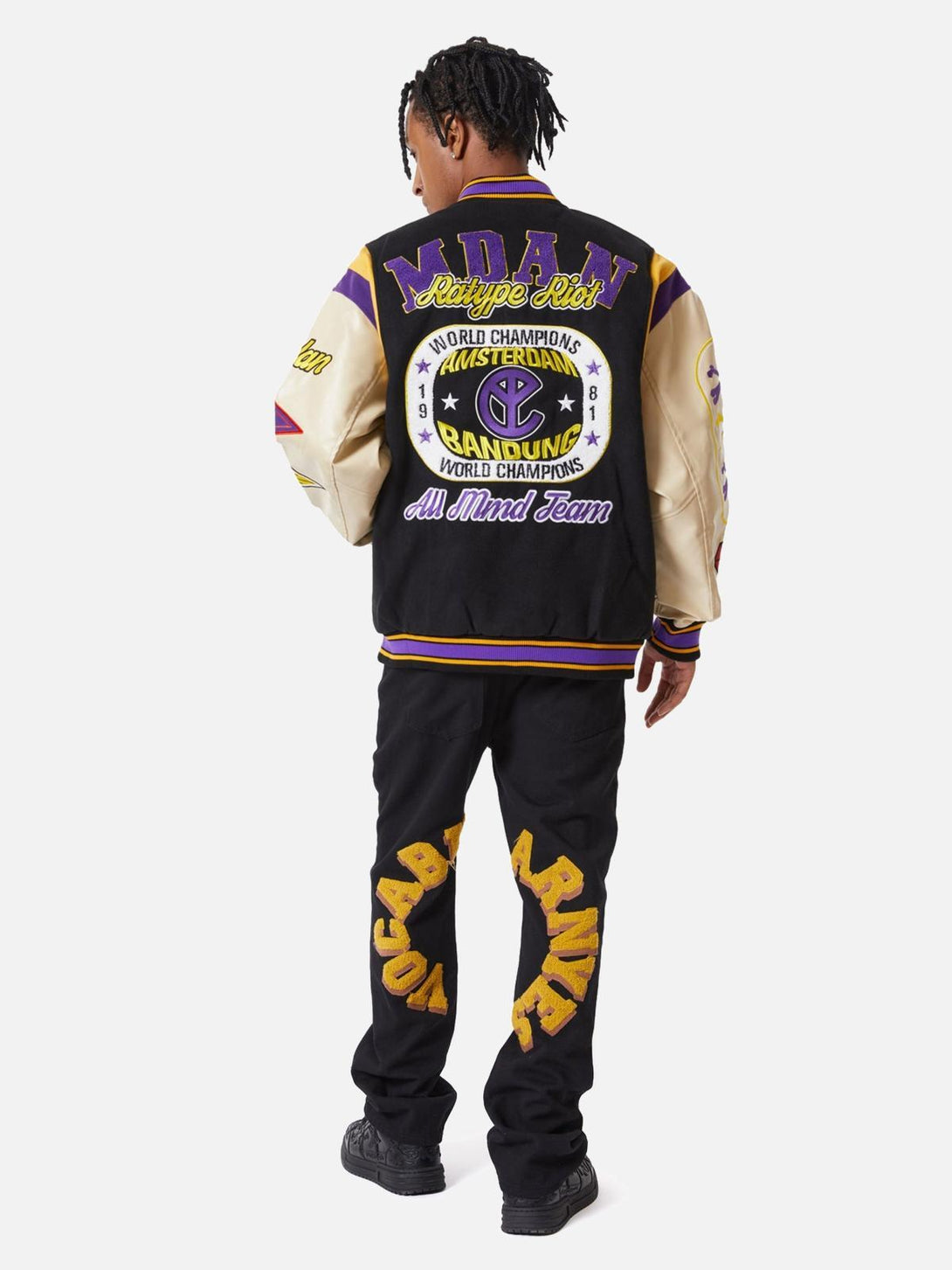 Back view of TALISHKO varsity jacket and jeans, highlighting bold patches and lettering.