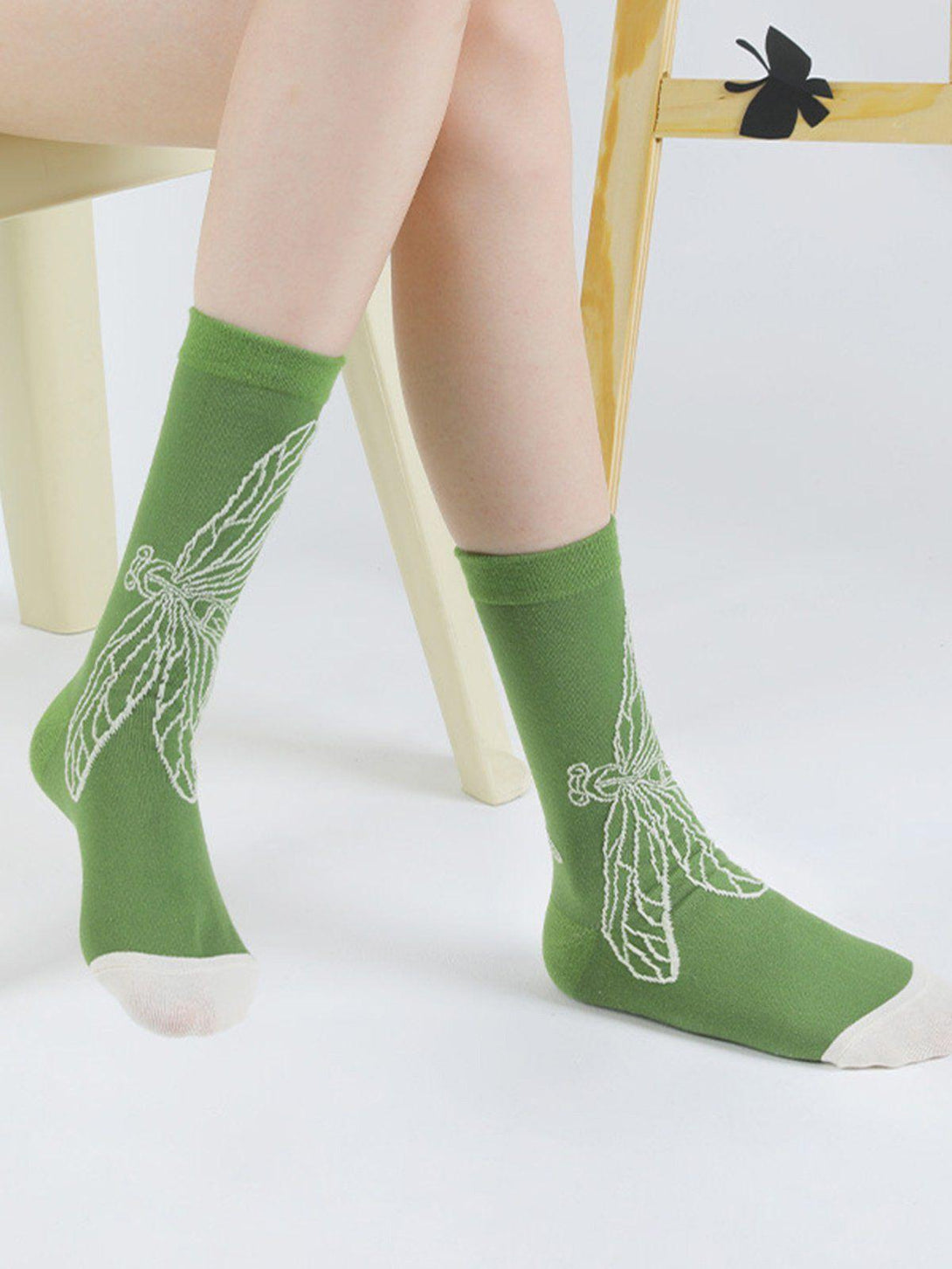 Green mid-calf socks with dragonfly design, worn seated, offering a fresh style by TALISHKO.