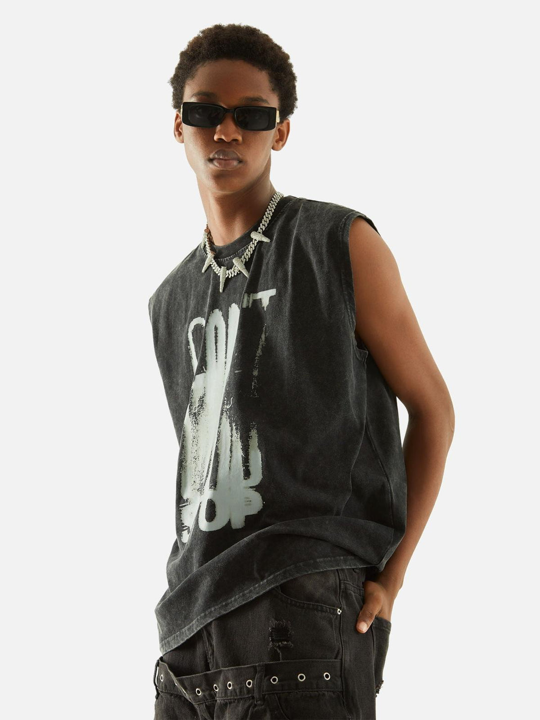 Model in a TALISHKO distressed vest with bold lettering, paired with dark jeans and sunglasses.
