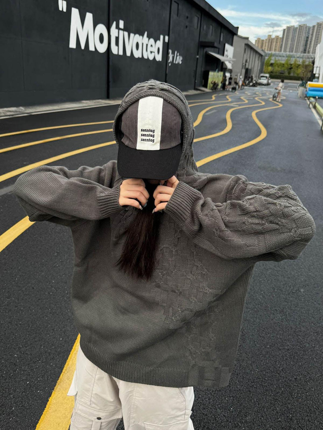 Person wearing a TALISHKO asymmetric knitted sweater hoodie with a cap, showcasing casual style.