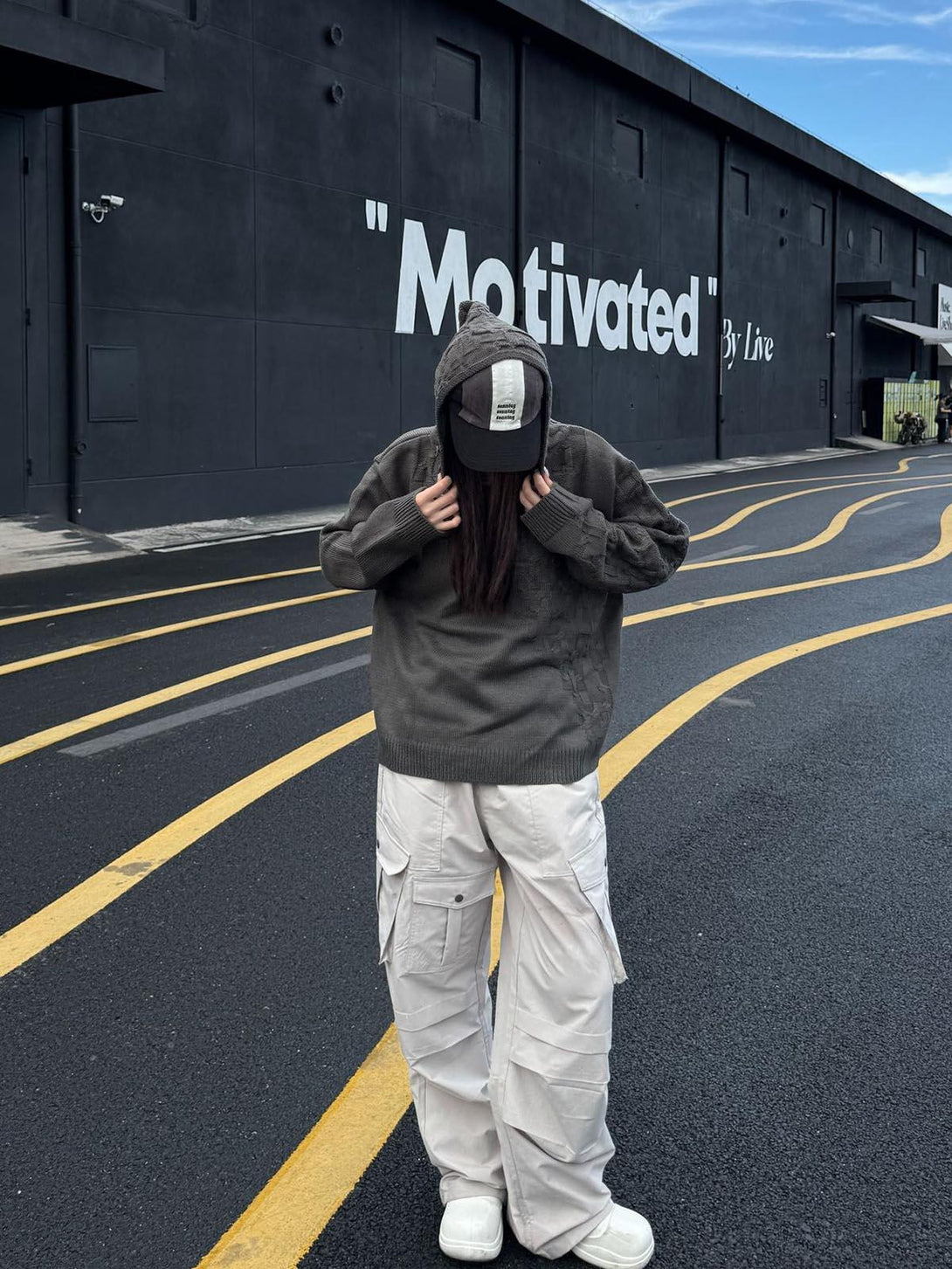 TALISHKO asymmetric knitted sweater hoodie worn with a cap and cargo pants, street style.