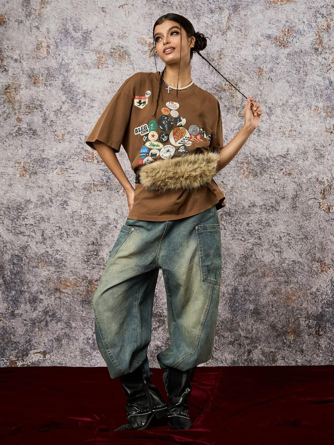 Model wearing a brown TALISHKO T-shirt with badge print, styled with loose jeans for a casual look.