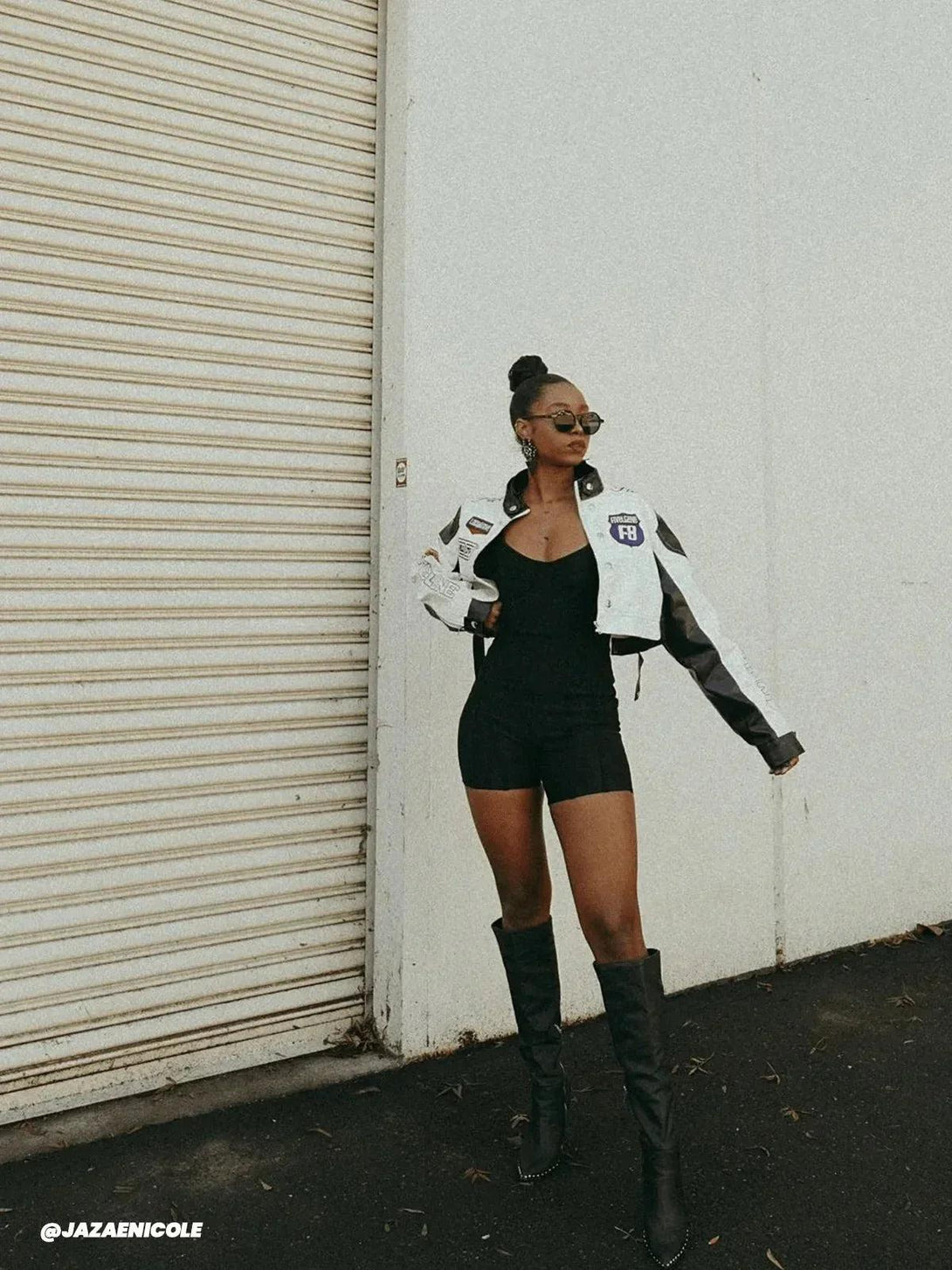 Model wearing TALISHKO's badge PU leather racing jacket over a sleek black outfit and boots.