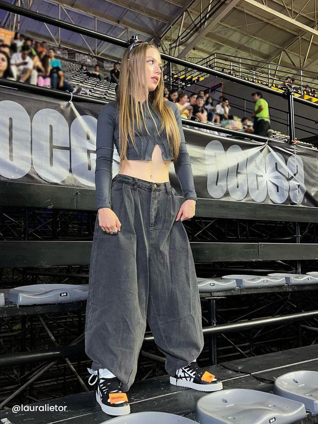 Model wearing TALISHKO baggy jeans, styled with a cropped top and sneakers at an indoor event.