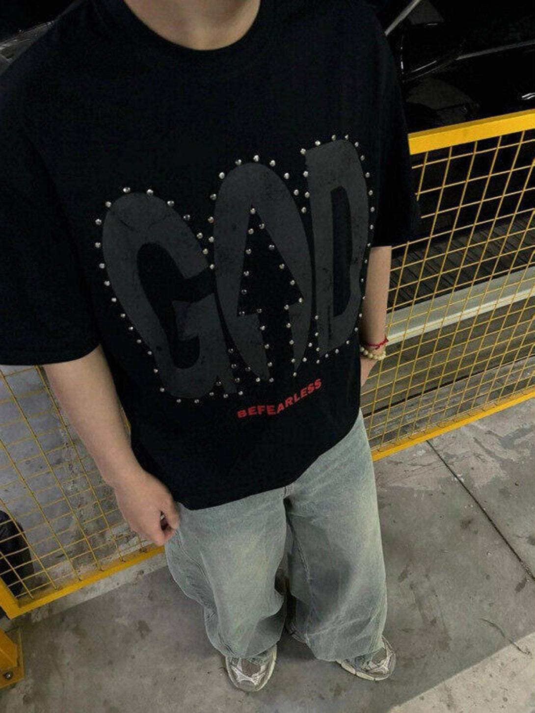 Model wearing a black TALISHKO T-shirt with bold slogan, paired with loose jeans and sneakers.