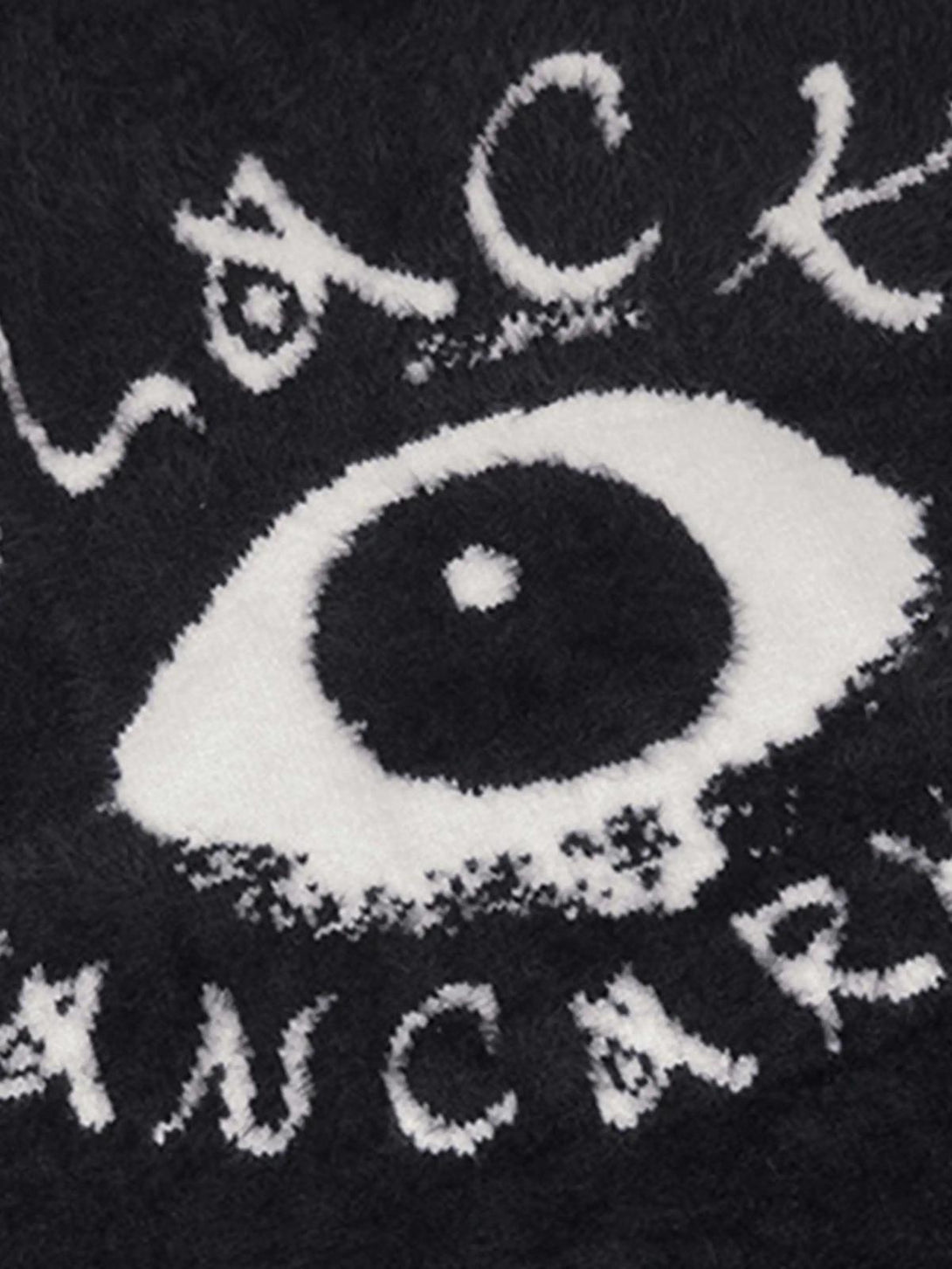A close-up of TALISHKO's black sweater, highlighting its bold eye pattern in textured detail.