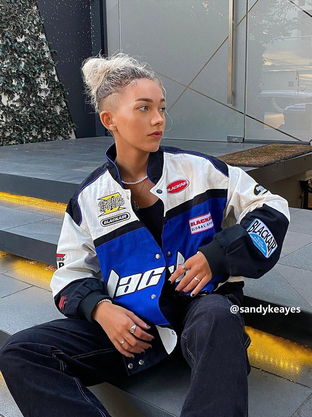 Model seated in TALISHKO BLACKAIR Motosports Jacket, showcasing bold racing-inspired style.