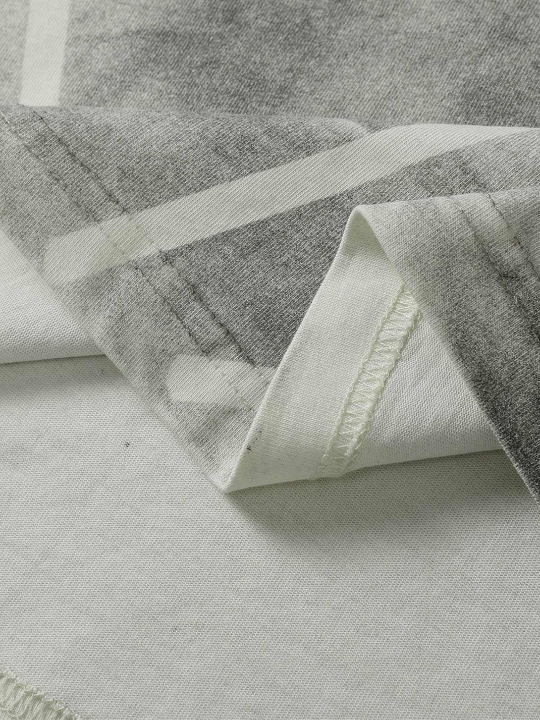 Detailed fabric and stitching of a TALISHKO oversized tie-dye T-shirt in gray tones.