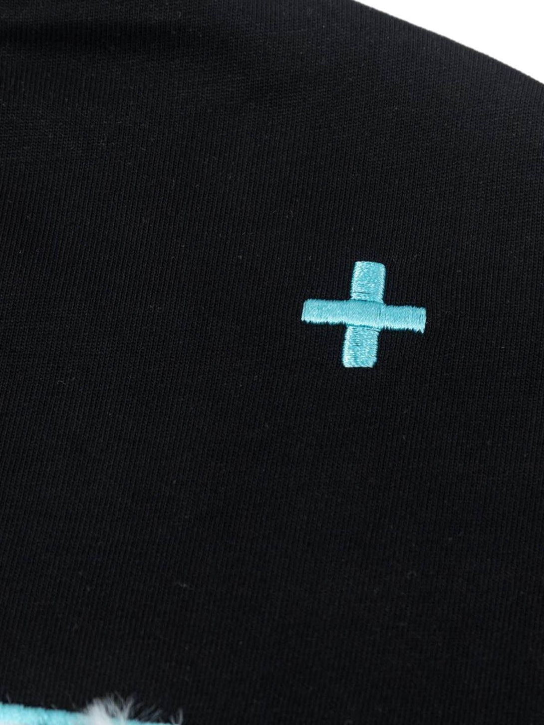 Detailed fabric and turquoise cross accent on a TALISHKO graphic T-shirt, highlighting texture.
