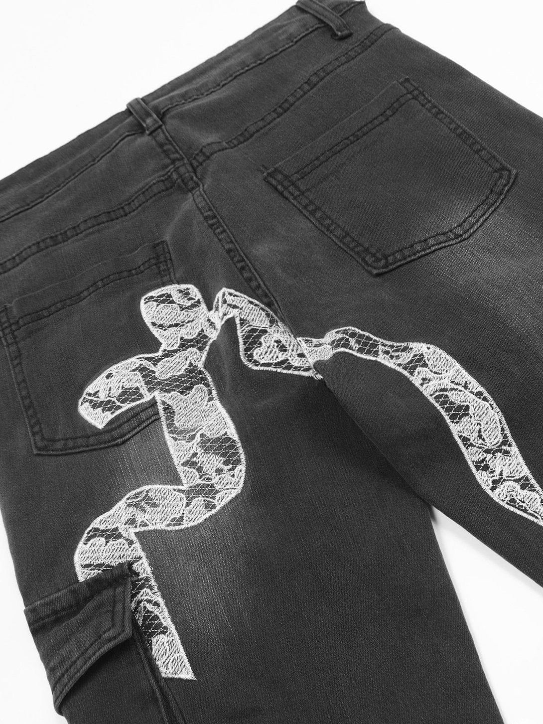 A detailed view of TALISHKO's washed jeans, highlighting the lace snake embroidery on the back.