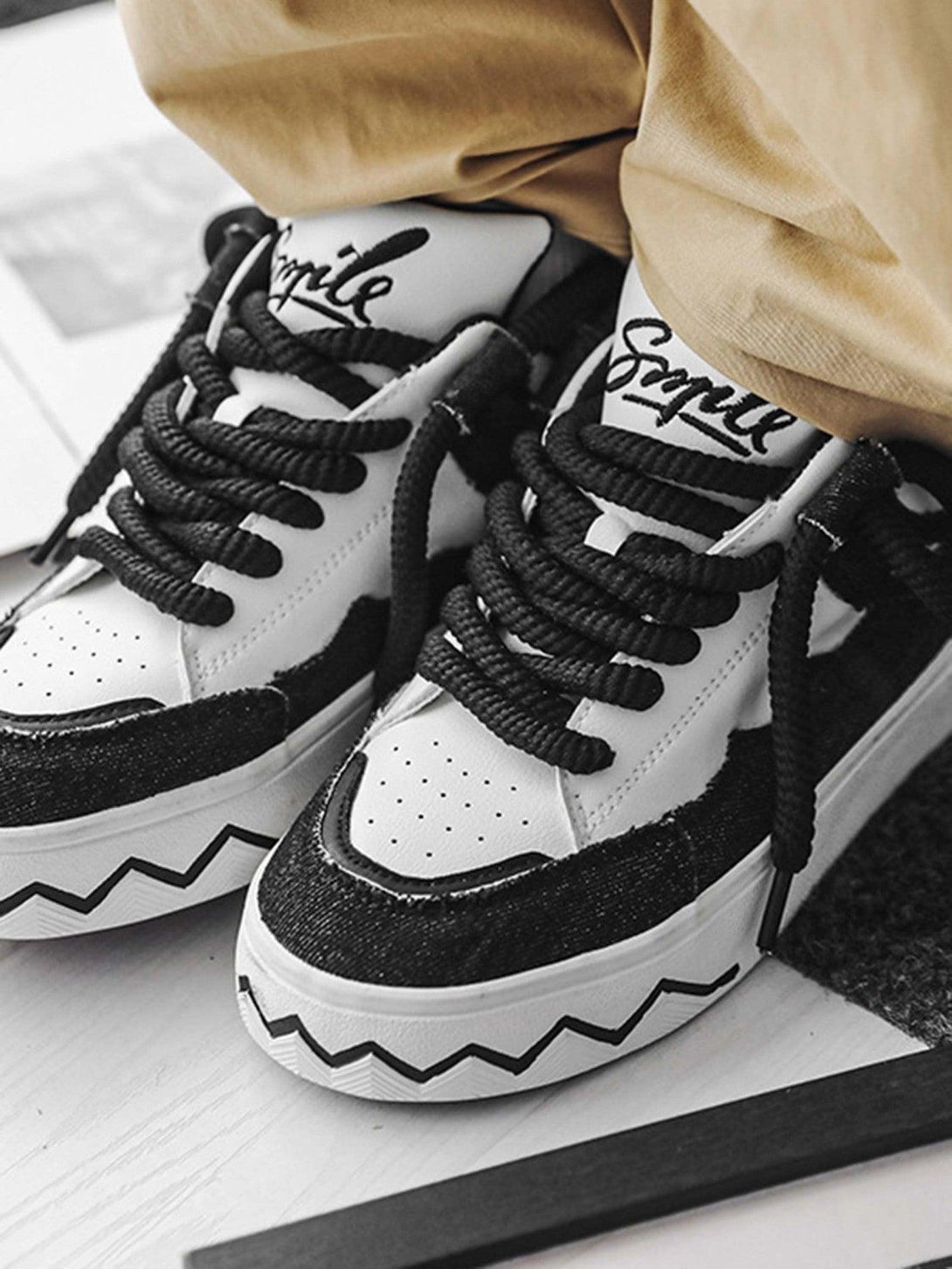 TALISHKO canvas sneakers with black-white contrast and zigzag sole detail, styled with beige pants.