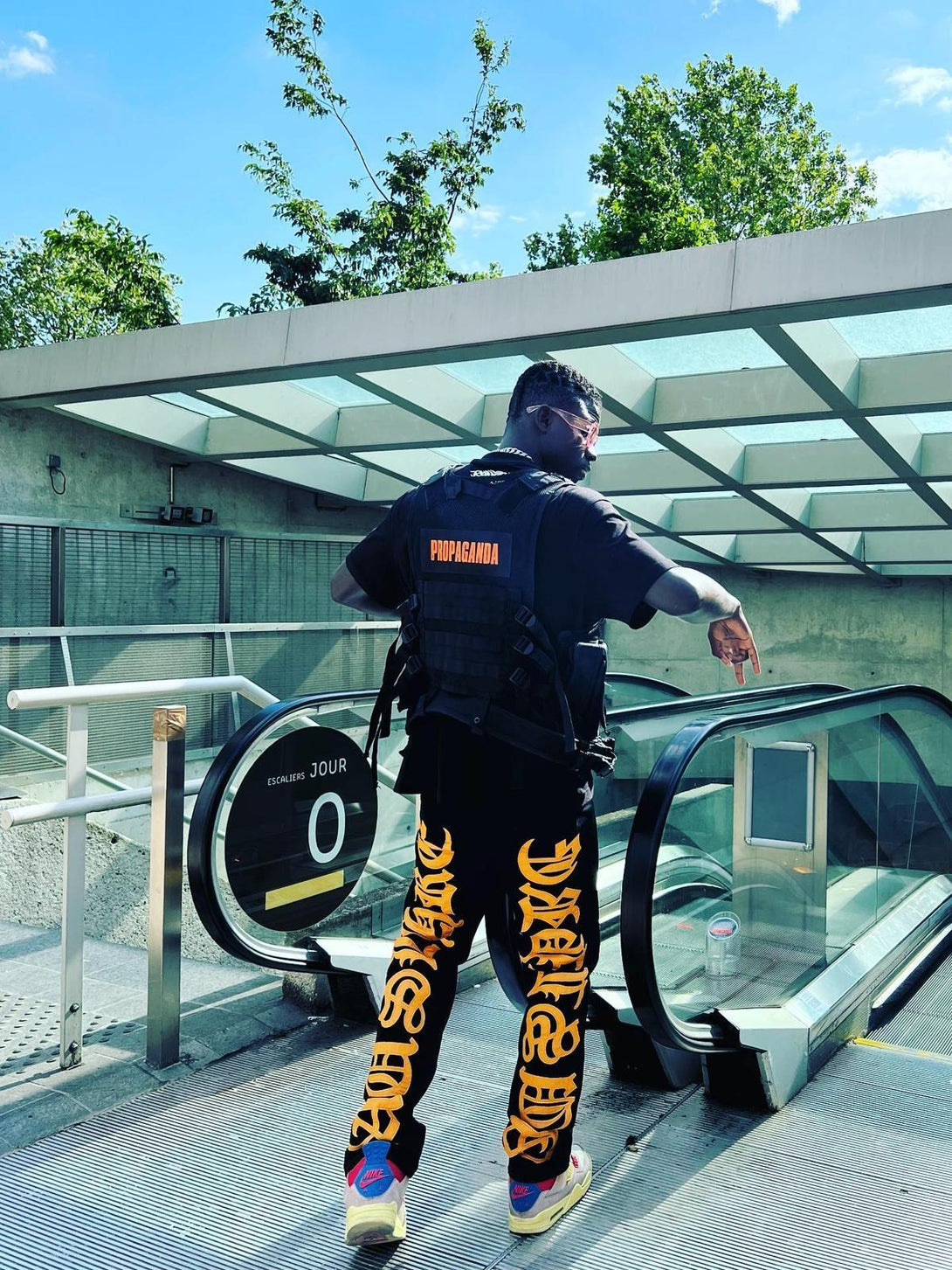 Model showcasing TALISHKO jeans with bold orange embroidery, paired with a black tactical vest.