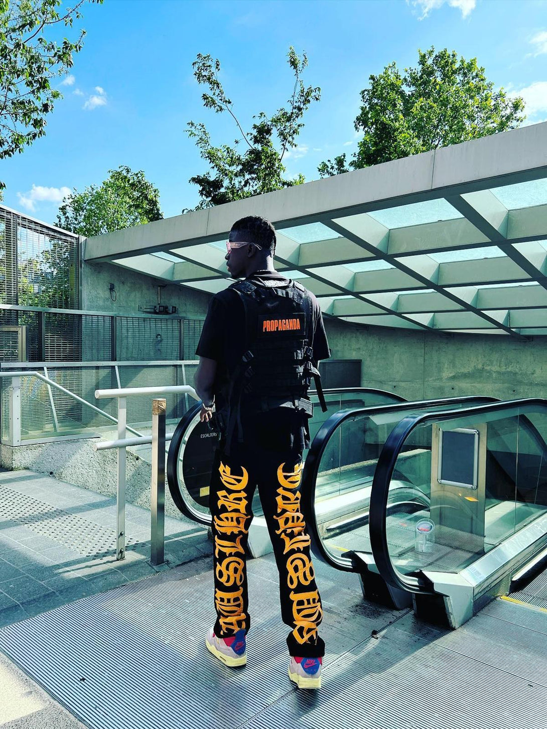 Model wearing TALISHKO jeans with striking orange embroidery, paired with a black vest.