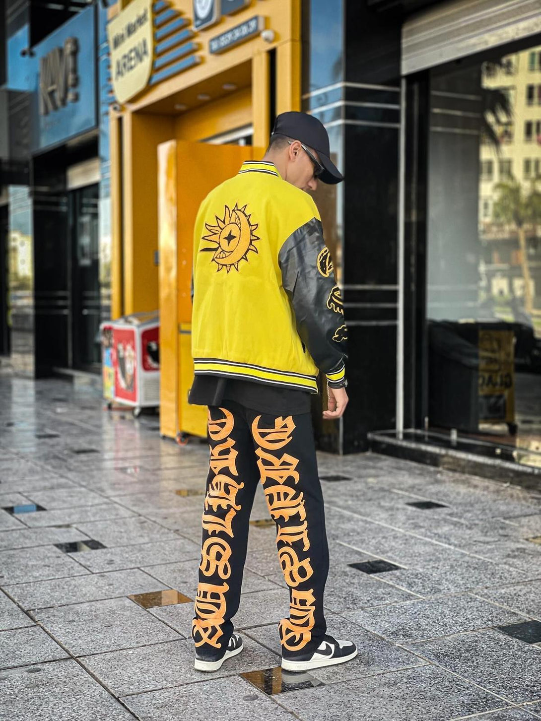 Back view of TALISHKO jeans with bold orange embroidery, paired with a vibrant yellow jacket.