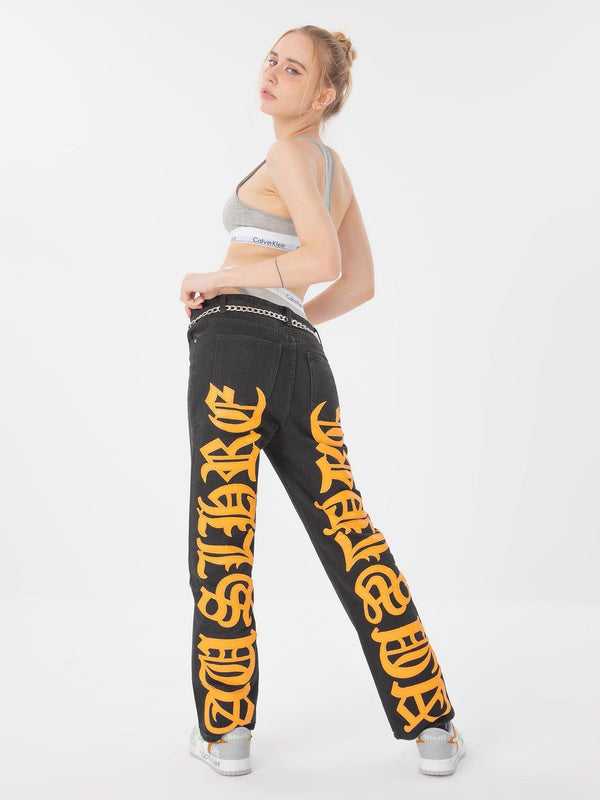 Model wearing TALISHKO black jeans with bold orange embroidered text, styled with a sporty top.
